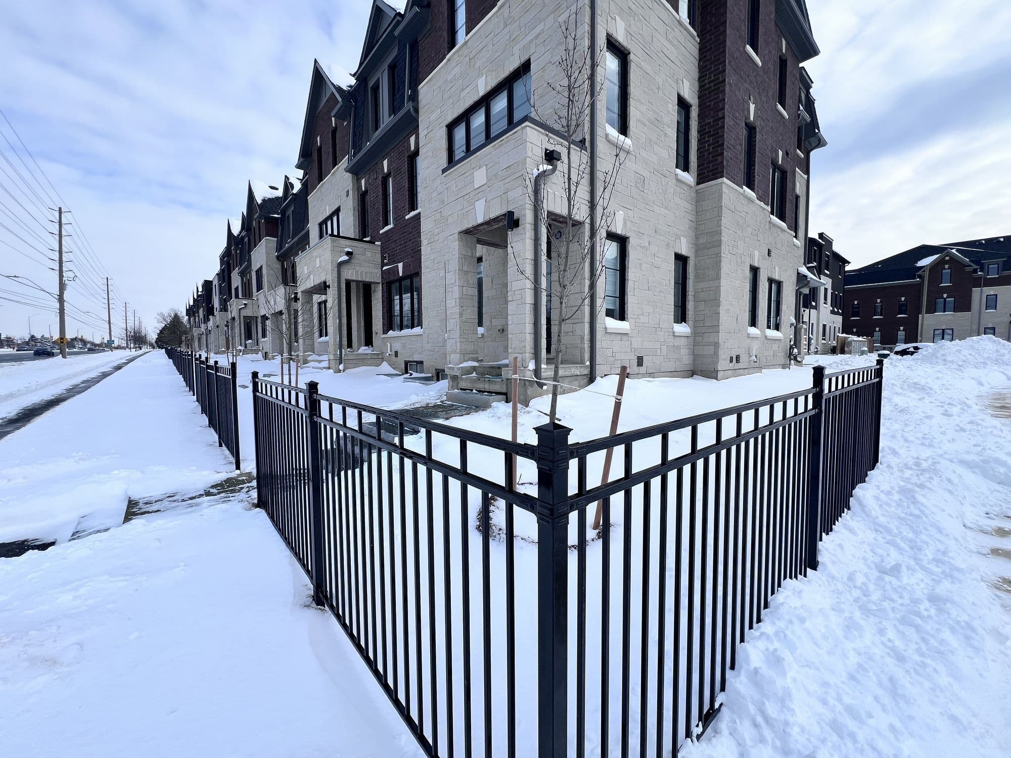 A row of new brick and stone townhouses in Mississauga under snow, behind a black iron fence, with a cleared path running alongside and a clear blue winter sky.
